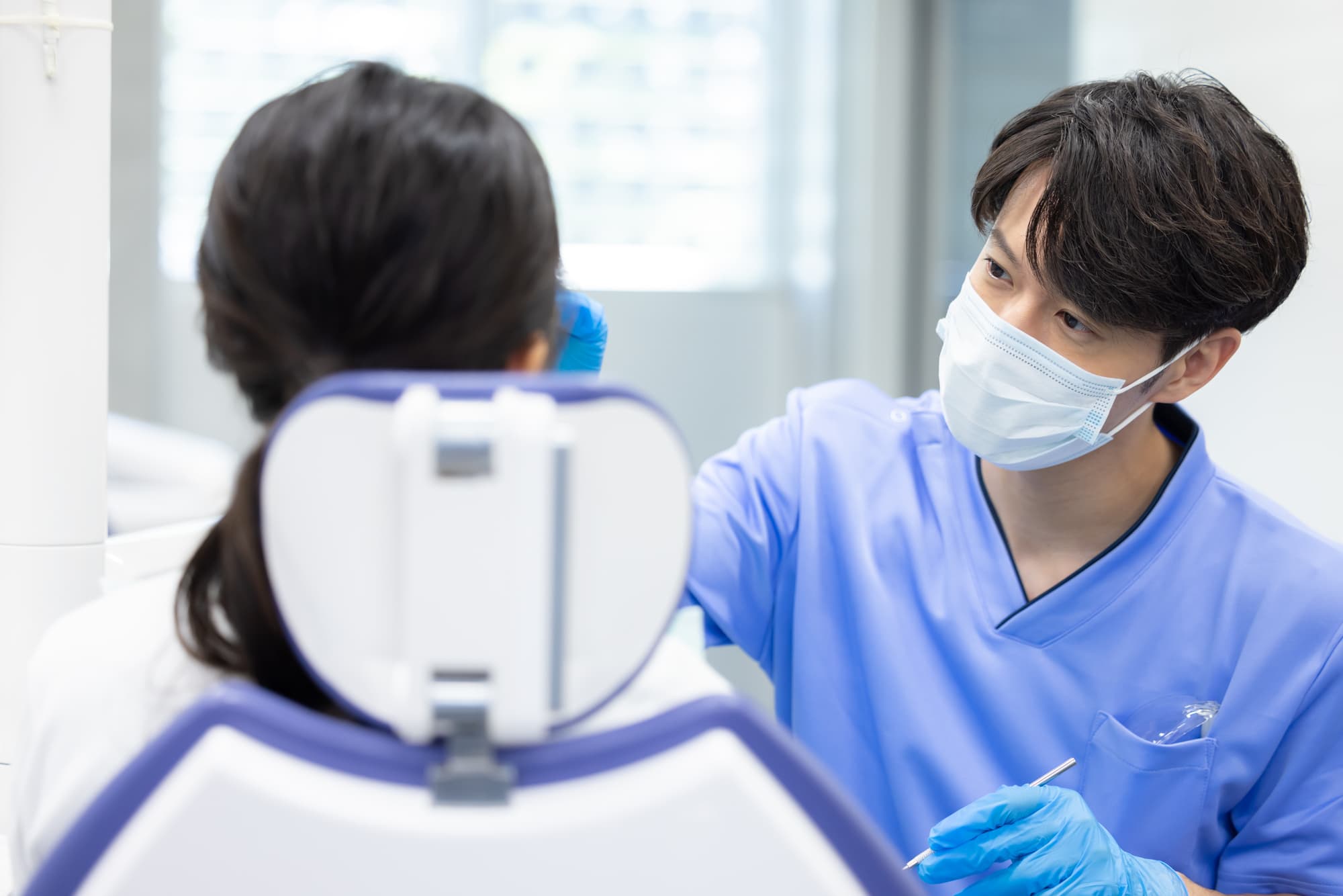 歯ぎしりで割れたセラミックの歯を歯科医に確認してもらっている患者